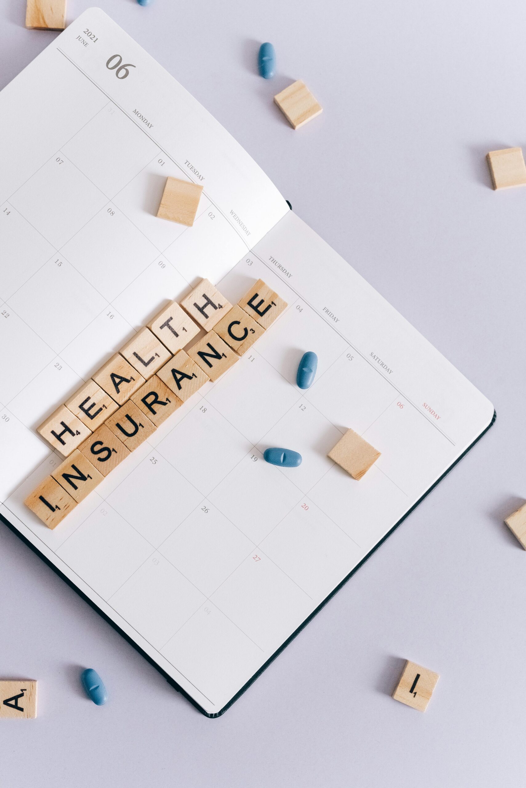 Top view of a planner with wooden tiles spelling 'health insurance' and scattered pills.